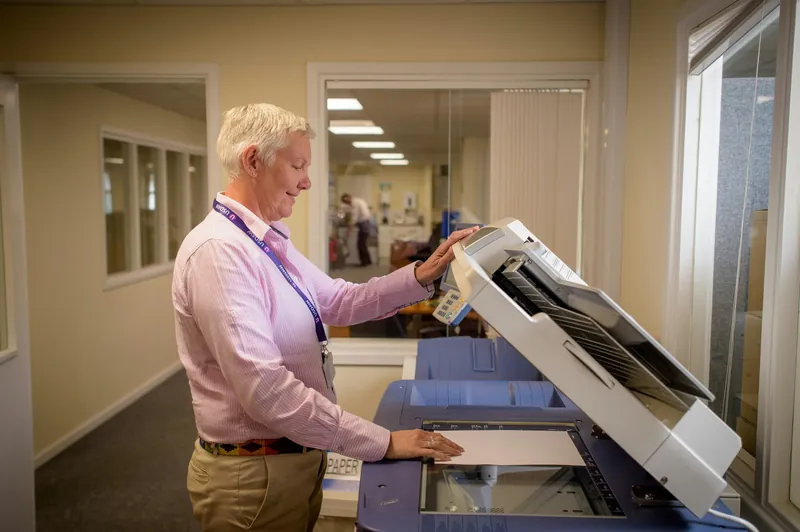 An office worker lifting the lid of a copier to scan a document